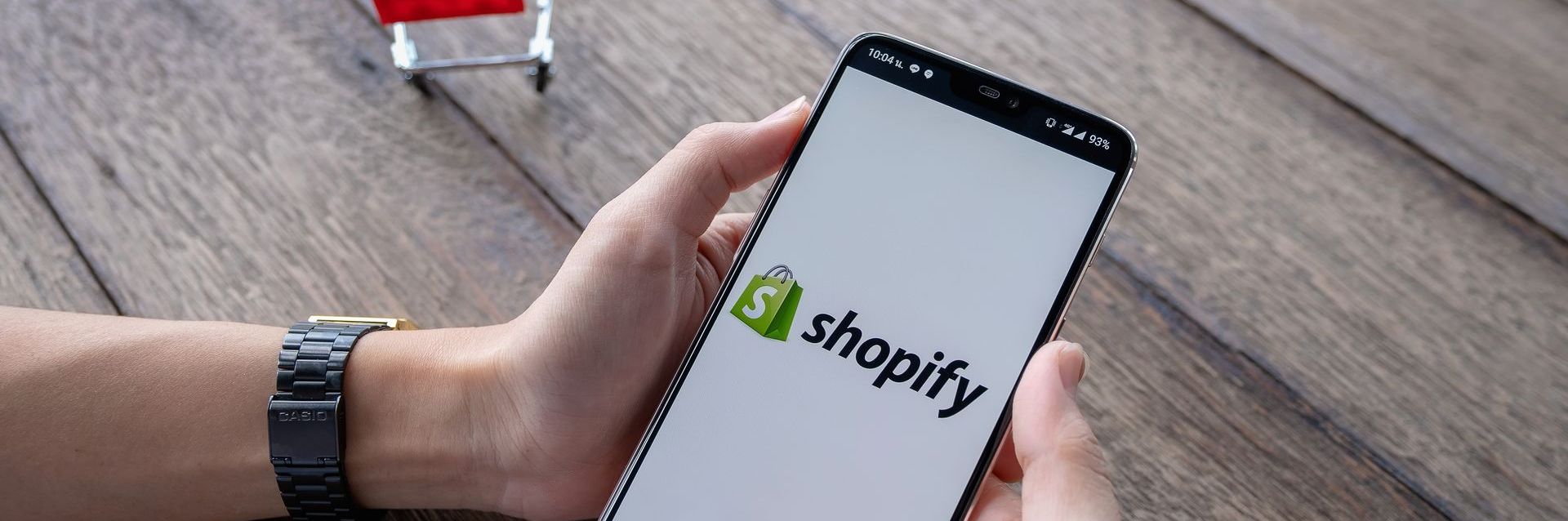 person holding phone with Shopify app and little trolley