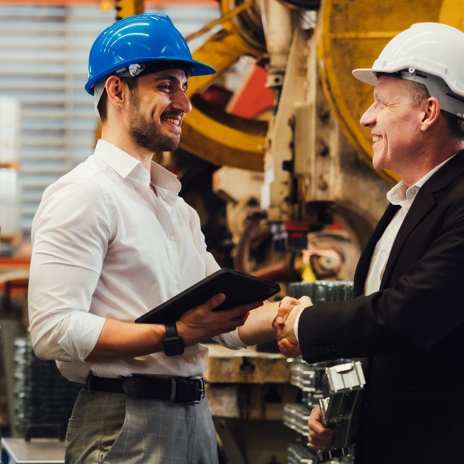 Two men wearing hard hats are shaking hands in a factory