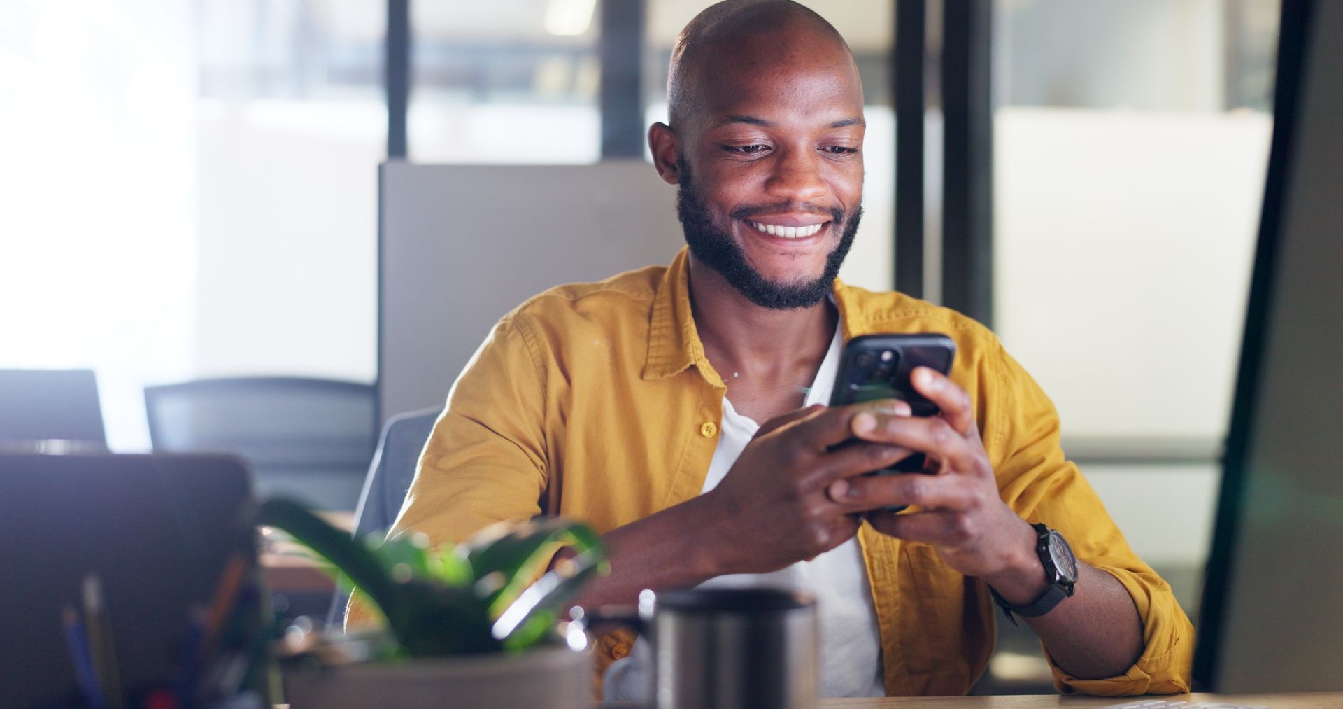 Man in yellow shirt sitting on phone looking happy