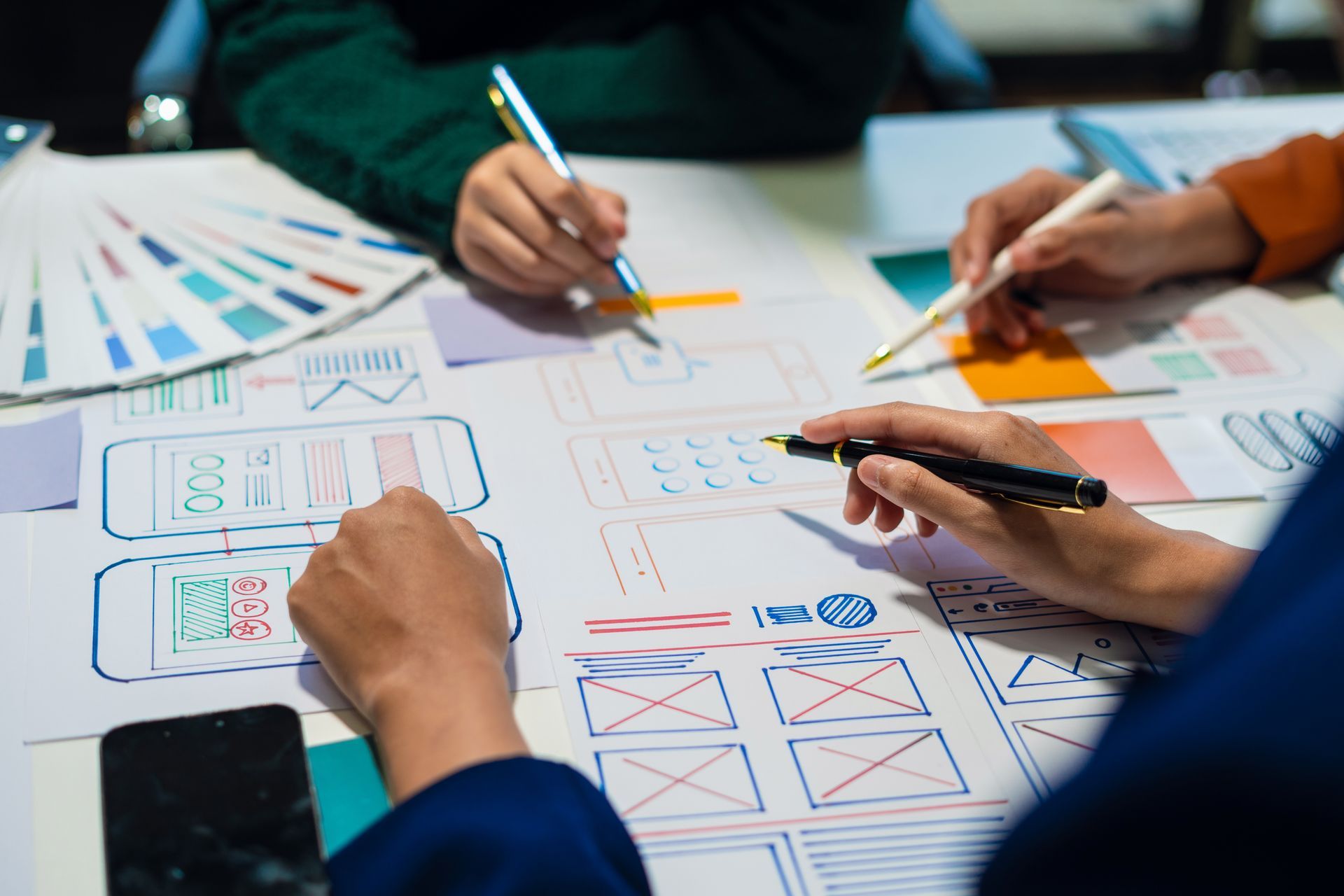 A group of people are sitting at a table drawing on a piece of paper.