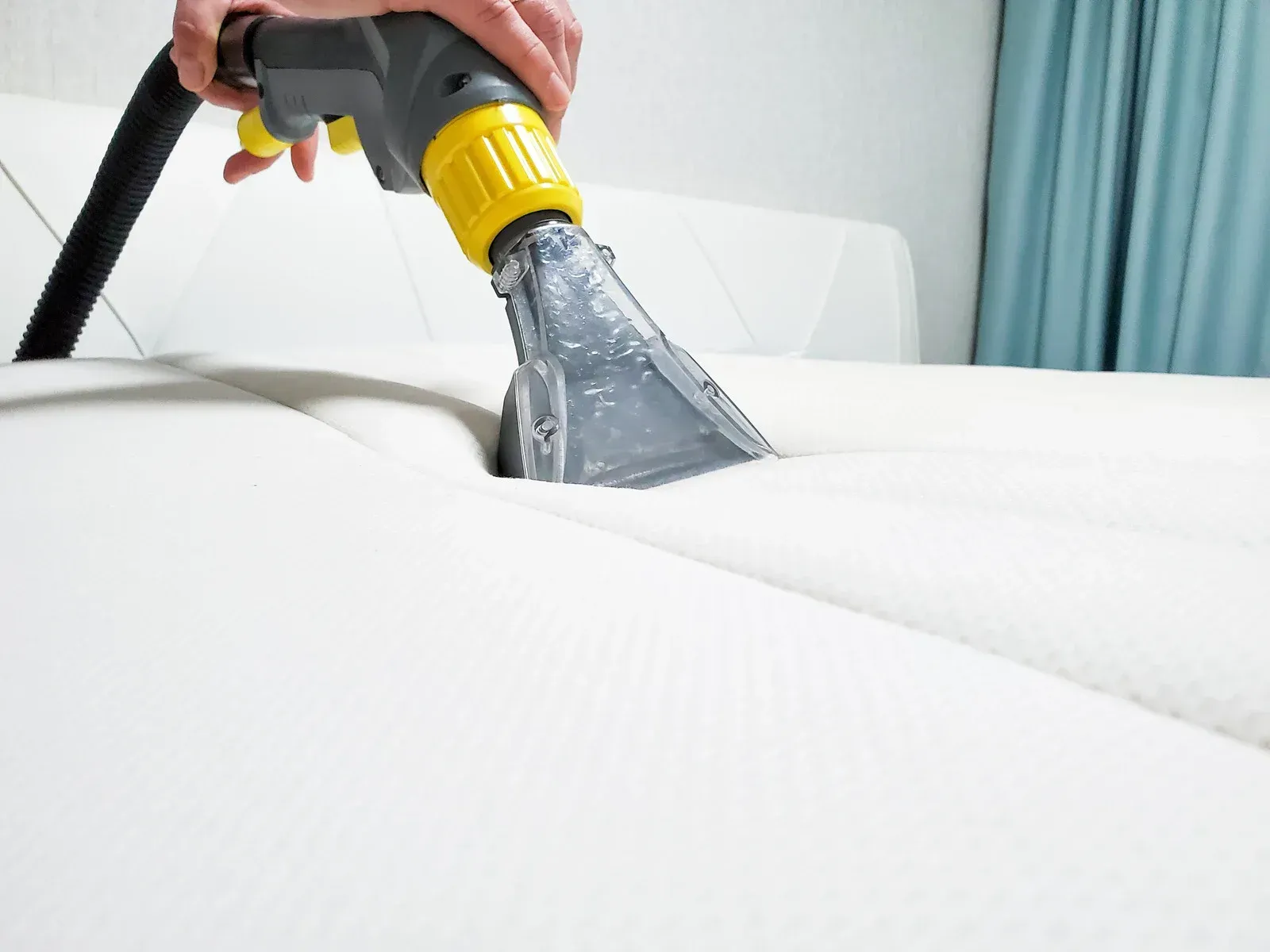 Person using a cleaning machine to sanitize a white mattress.