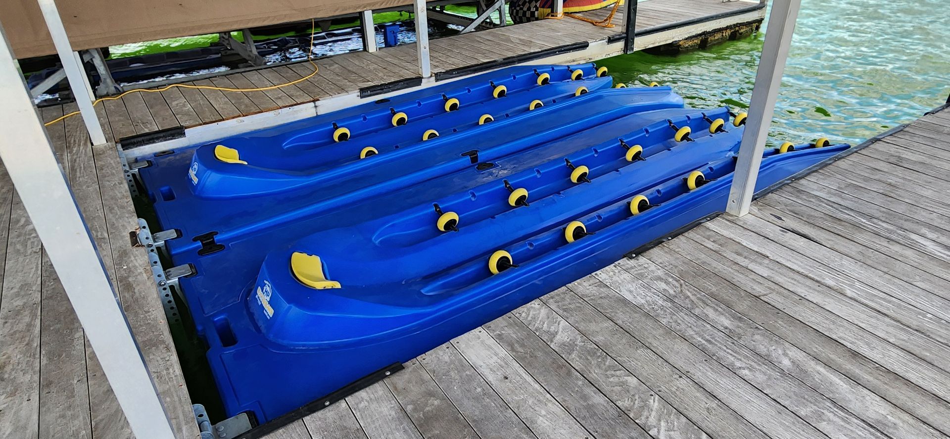 Blue kayak launch on a wooden dock, with yellow handles. White supports, water visible.