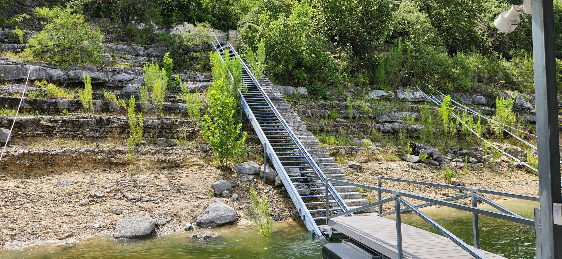 A metal ramp leading from a dock up a rocky hillside with vegetation.