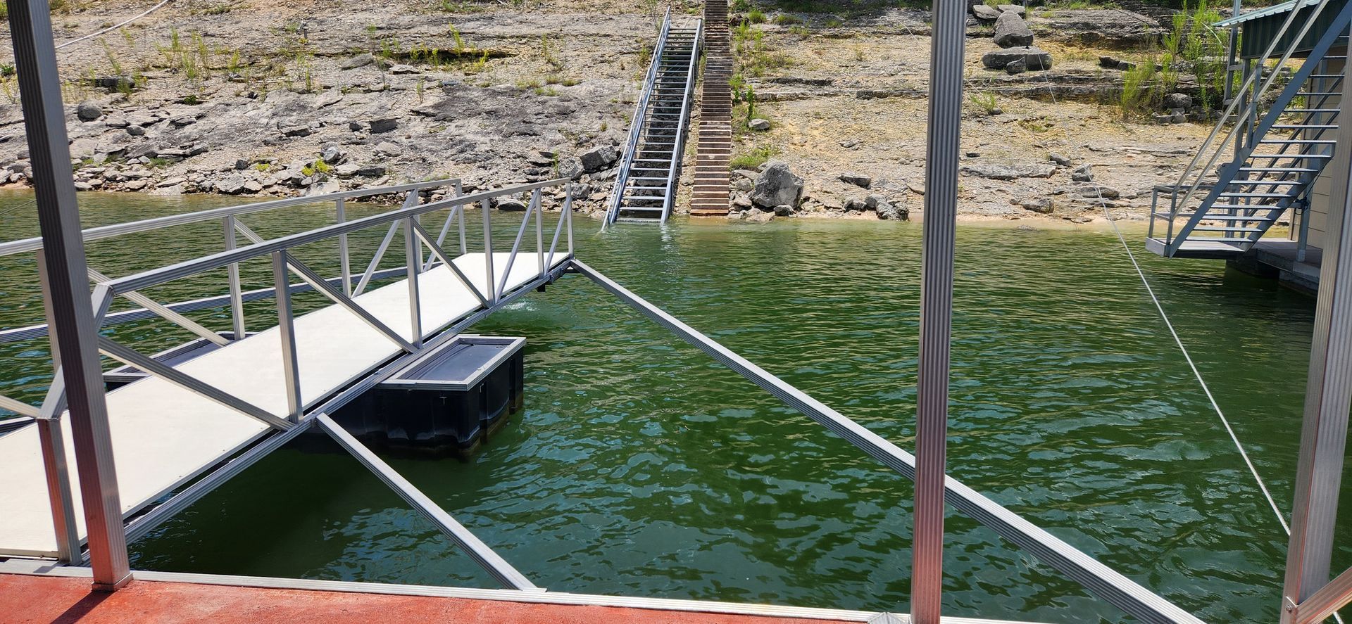 Dock on a lake with stairs leading up to the shore. Green water.