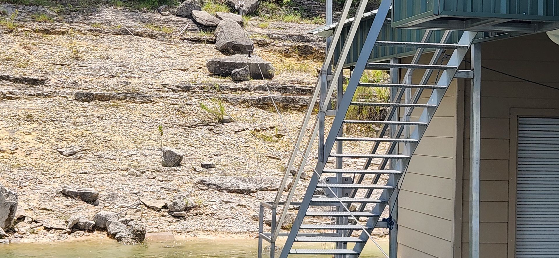 Metal stairs on a building by a rocky, dry bank. Water is in the foreground.