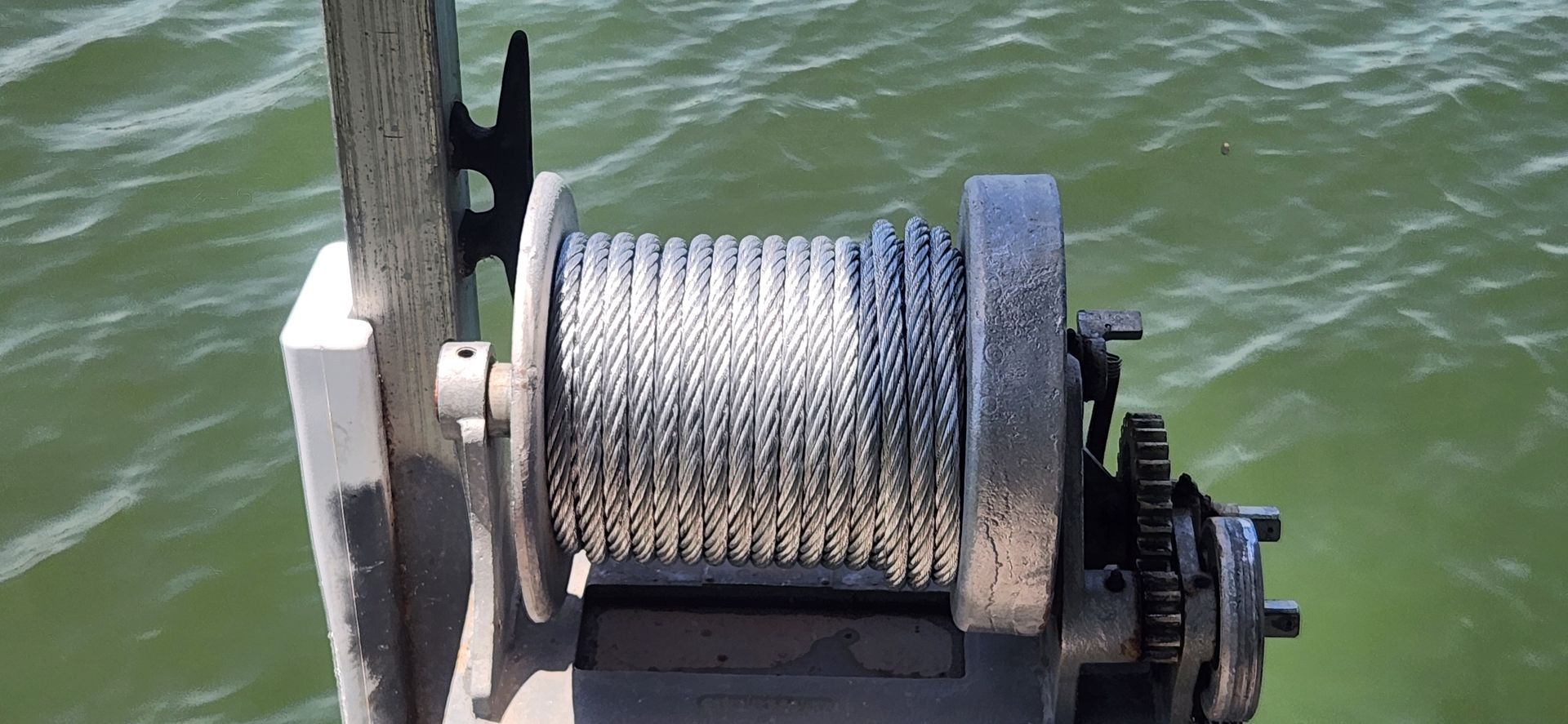 A winch with a steel cable, attached to a wooden post, with water in the background.