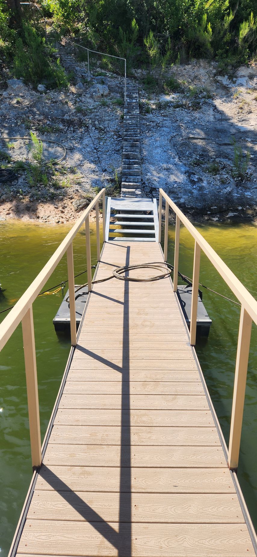 Wooden dock with handrails leads to a staircase ascending a rocky hillside.
