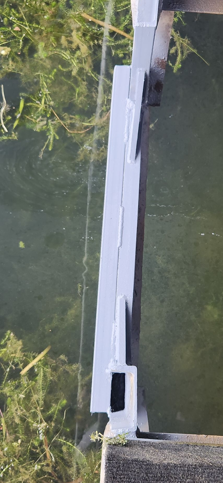 Metal structure over water, possibly a bridge or dam. Green vegetation visible.