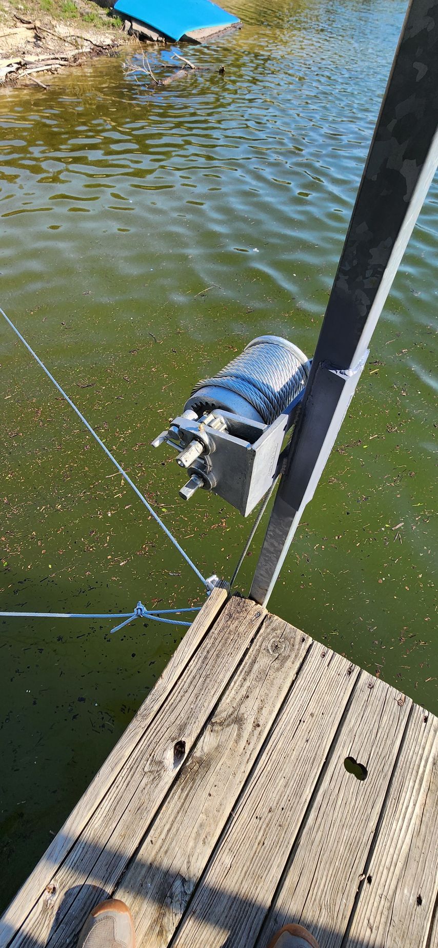 A wooden dock with a blue ramp in the background. A motor is attached to a post above the water.