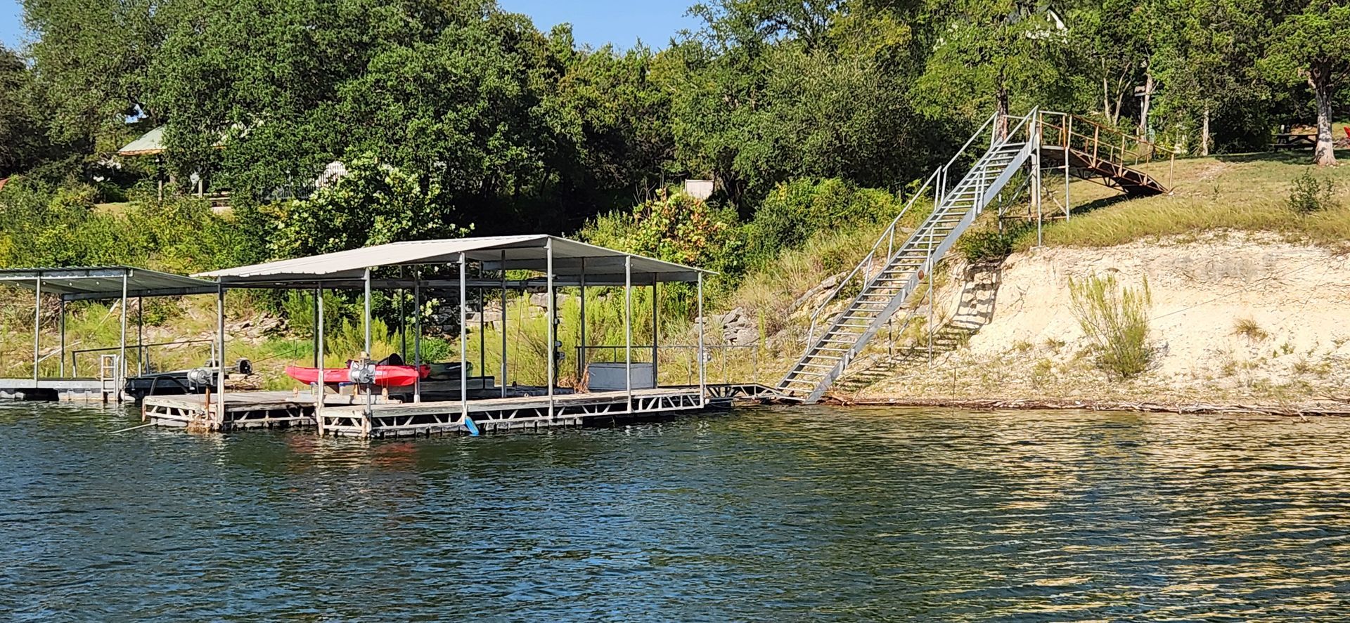 Dock with stairs leading up a grassy bank, surrounded by trees and water.