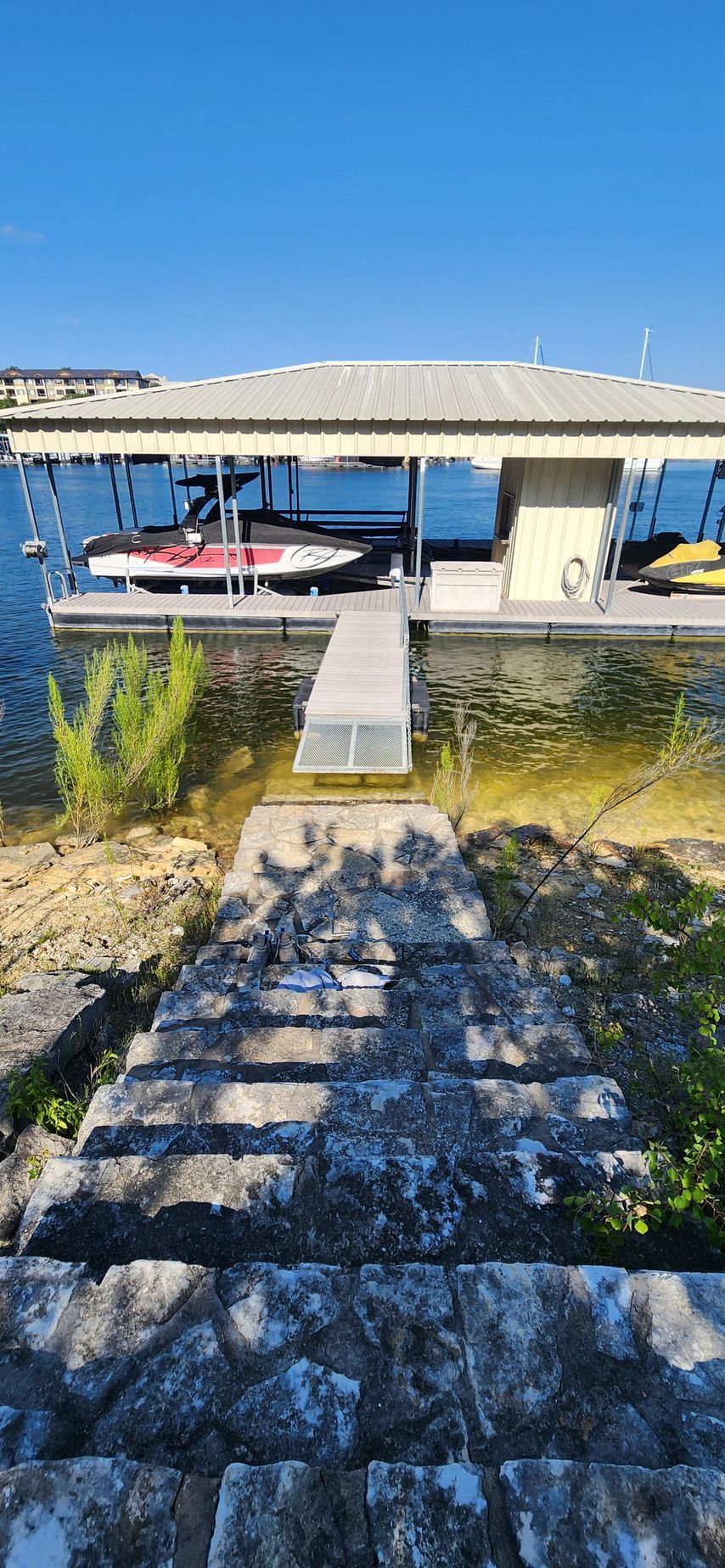 Stone steps lead to a boat dock with a boat under a roof, clear blue sky.