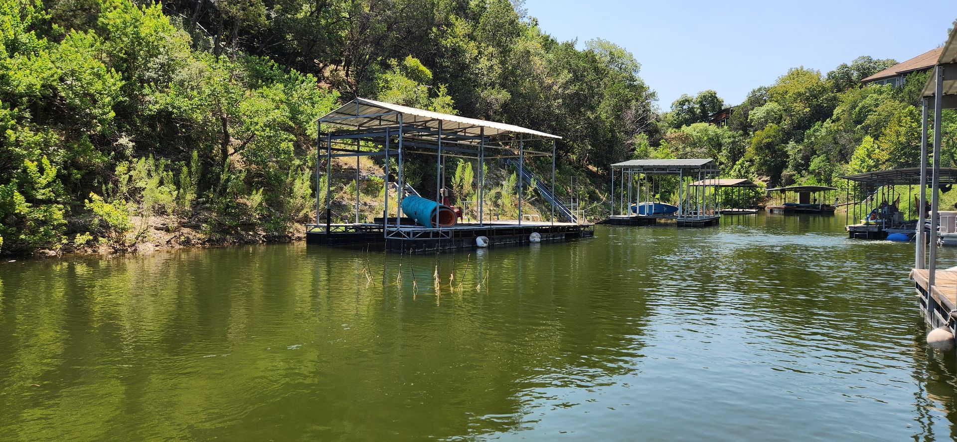 Pontoons and boats on a green lake surrounded by trees on a sunny day.