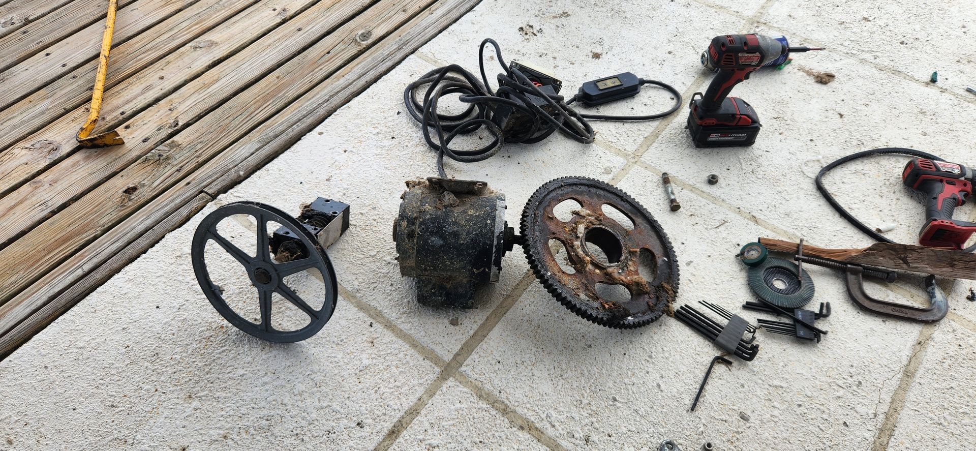 Deconstructed motor parts and tools on a concrete surface near wooden decking.