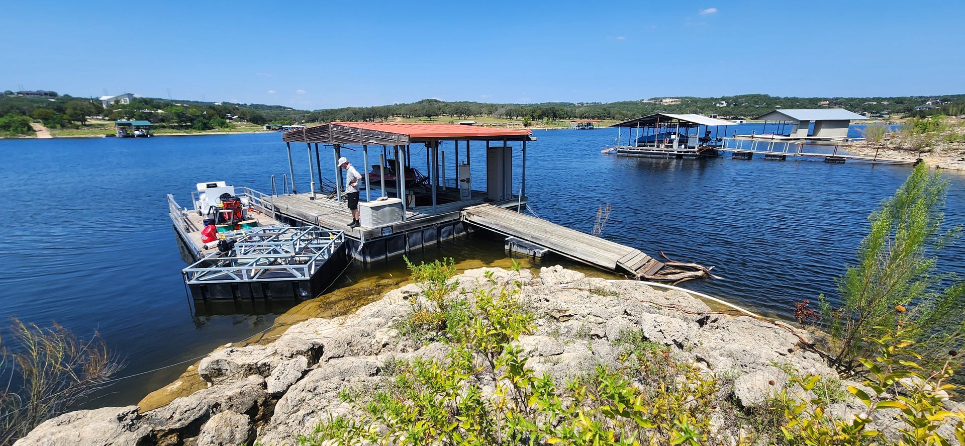 A pontoon boat tied to a dock on a lake under a blue sky.