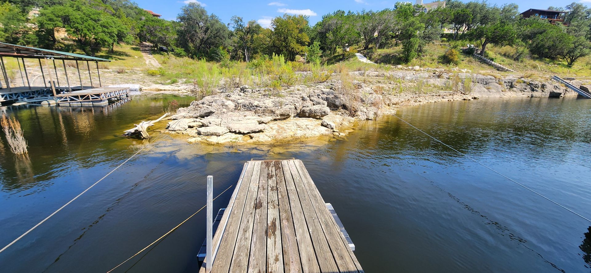 Wooden dock over dark water with rocky shore, trees, and a blue sky.