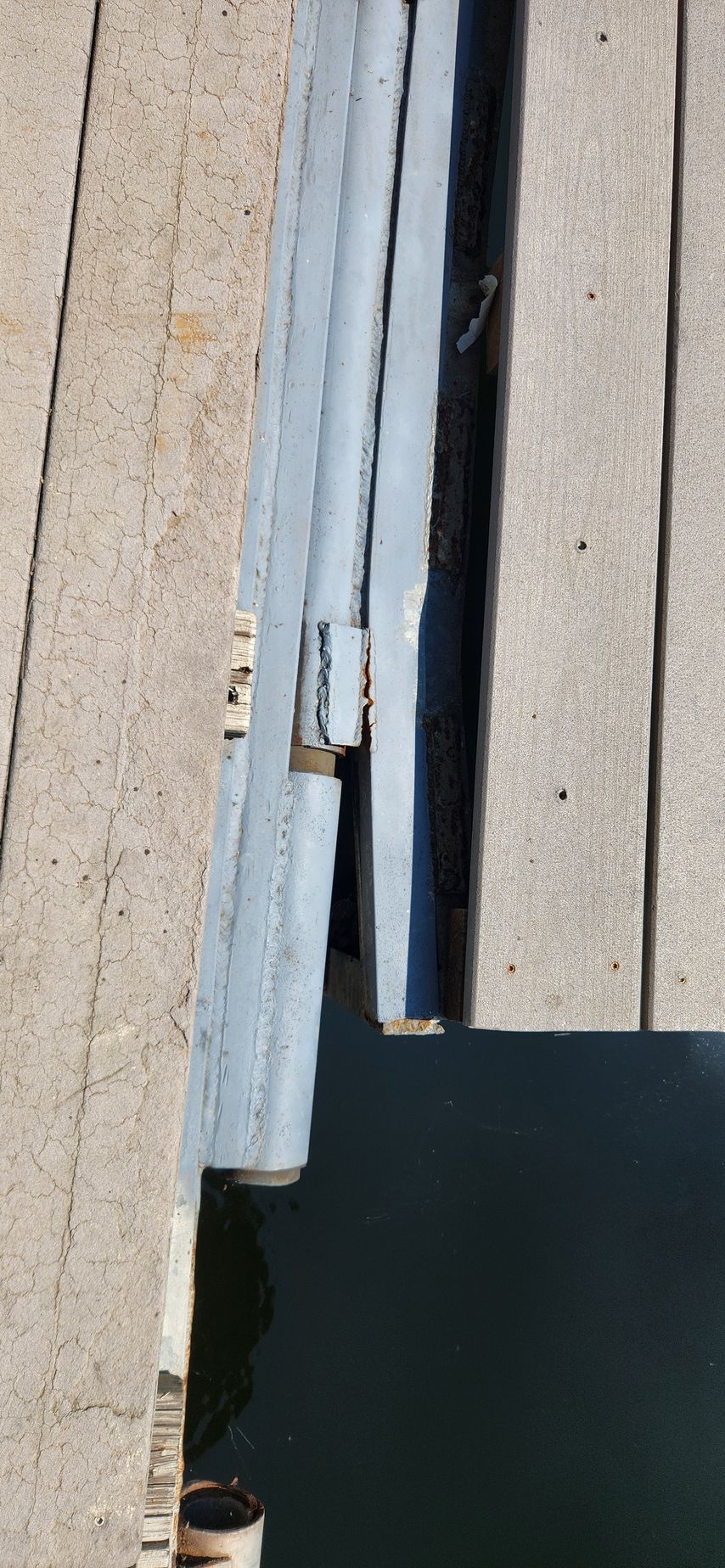 Dock planks with a grey, hinged, metal bar over dark water.