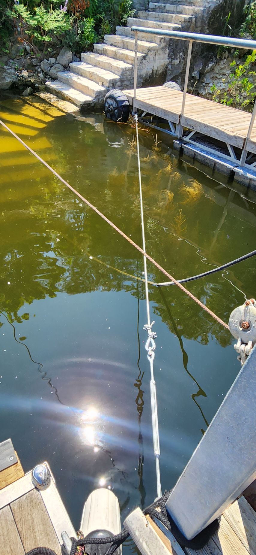 View of a dock, steps, and water. A shiny sun reflection is on the water.