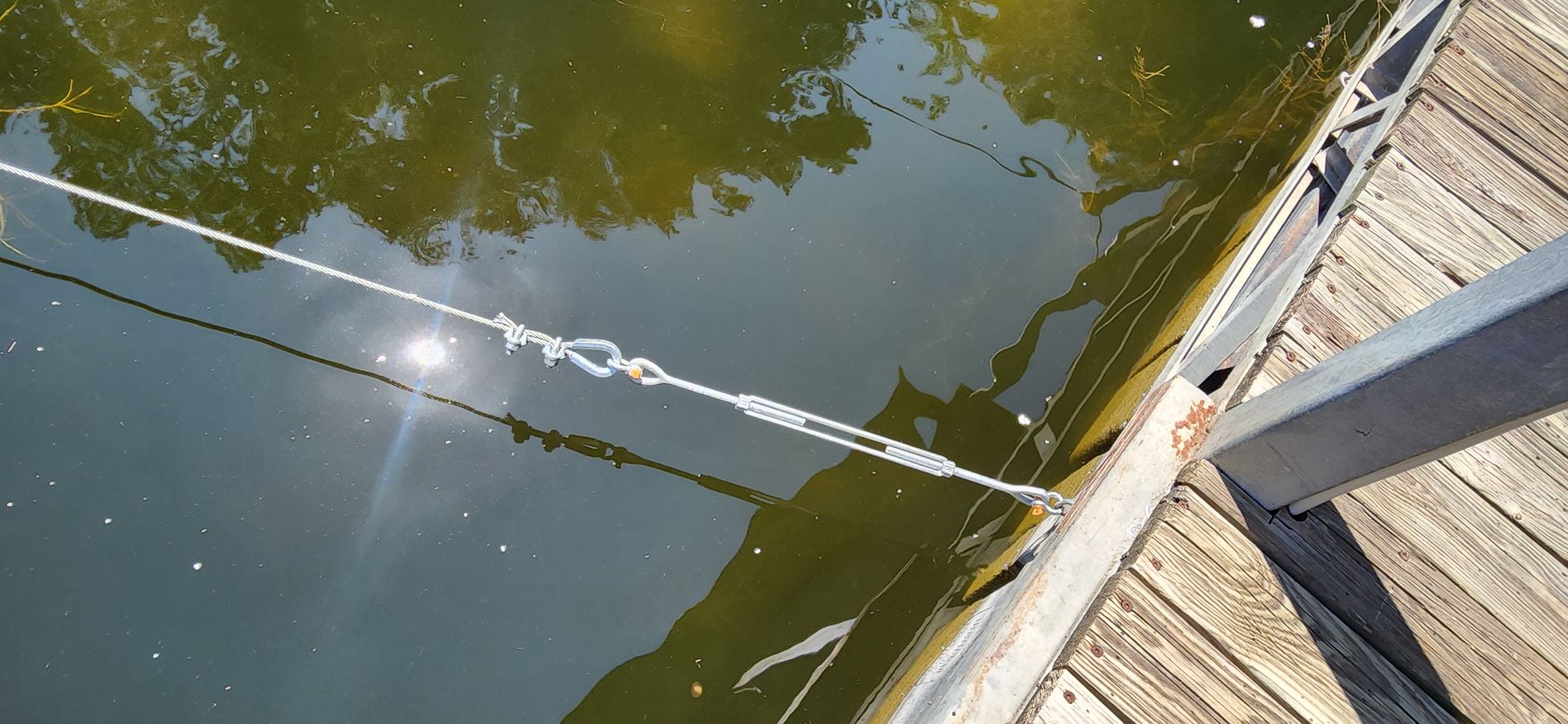 Rope tied to a wooden dock, suspended over dark water with sunlight reflecting.