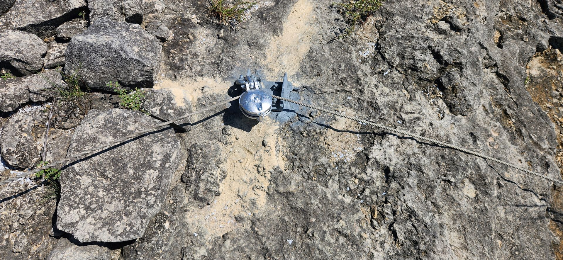 A metallic object on a rock surface with cracks and sand, possibly surveying.