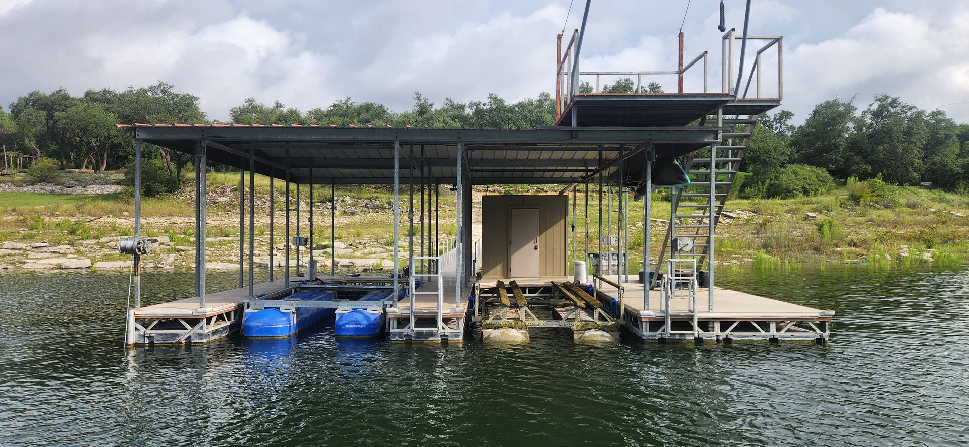 A waterside view of a lake from a boat dock with a visible covered dock in the distance and a clear sky.