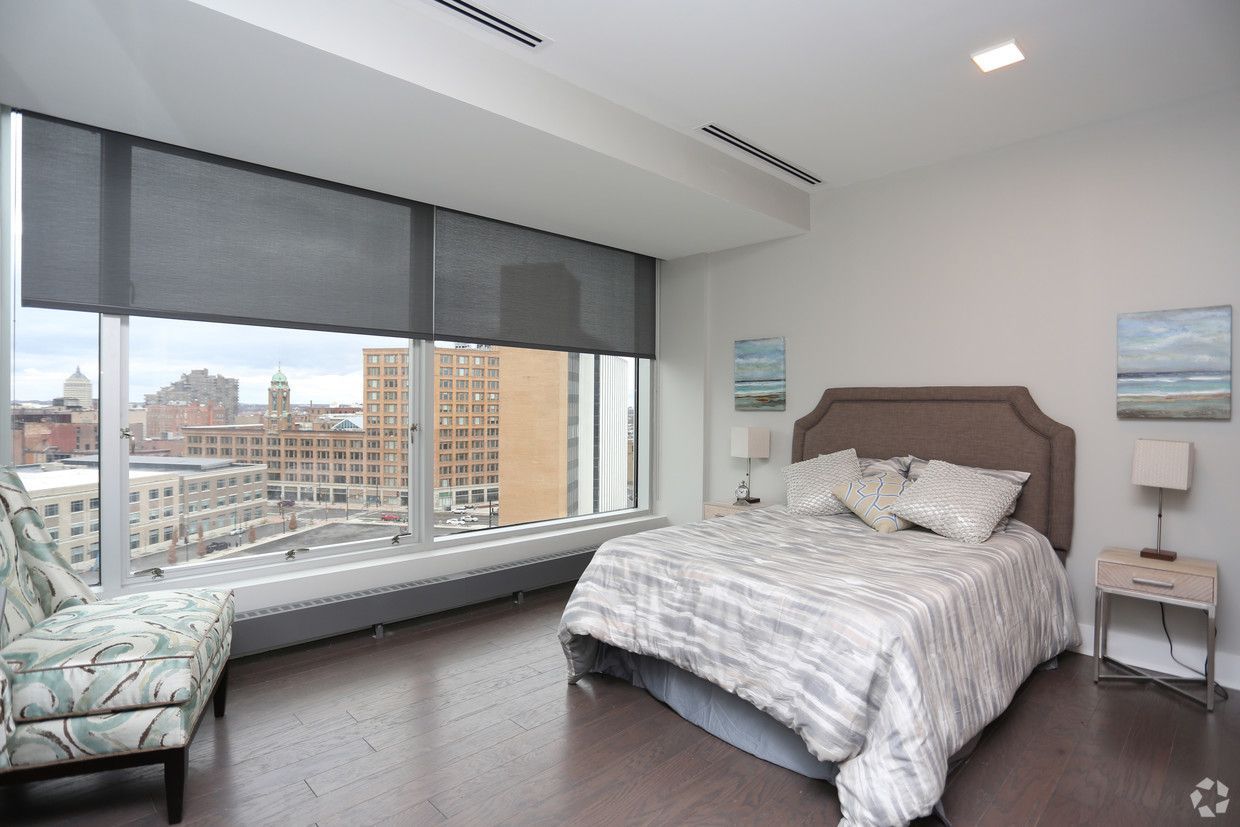 Bedroom with bed, chair, and large window overlooking city.