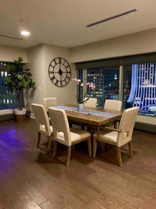 Dining room with a table, chairs, clock, and city view at night.