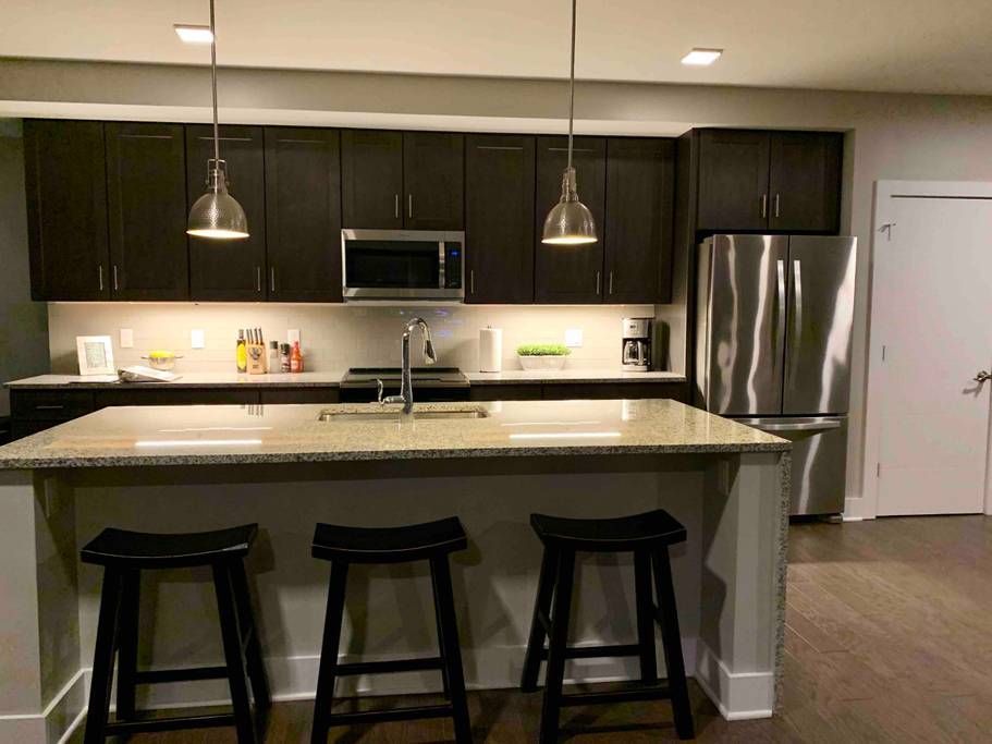 Modern kitchen with island seating, dark cabinets, stainless steel appliances.