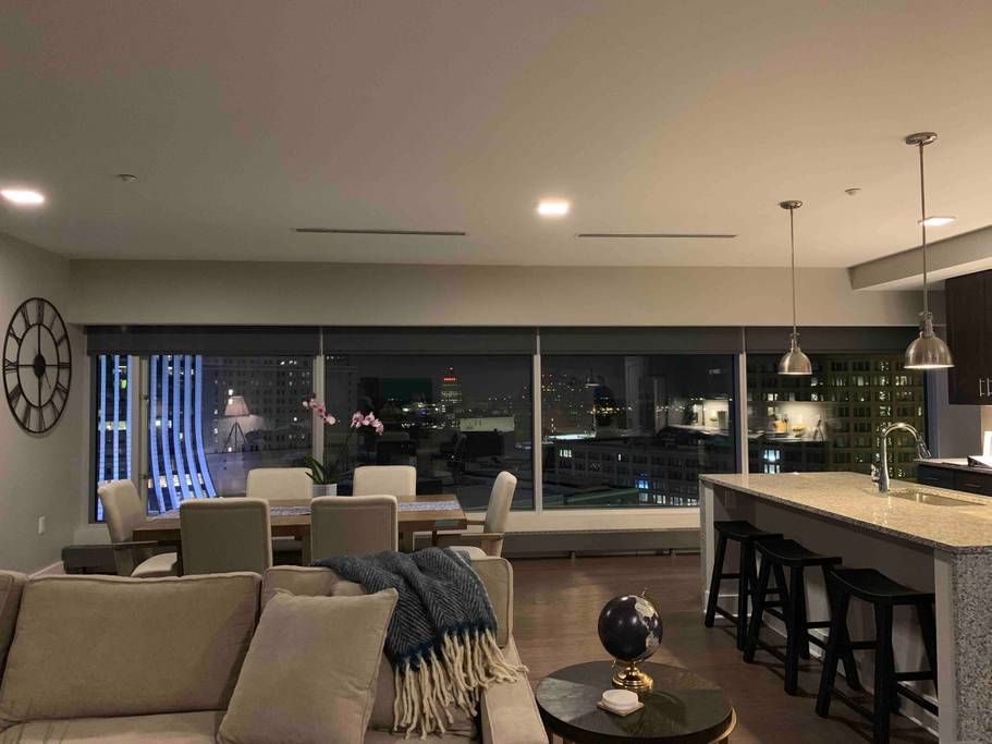 Cozy living room with city view at night, featuring a sofa, dining table, and kitchen island.