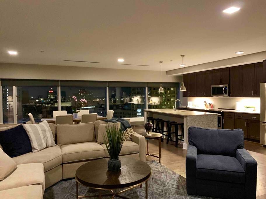 Open-concept living space with sectional sofa, kitchen island, city views at night.