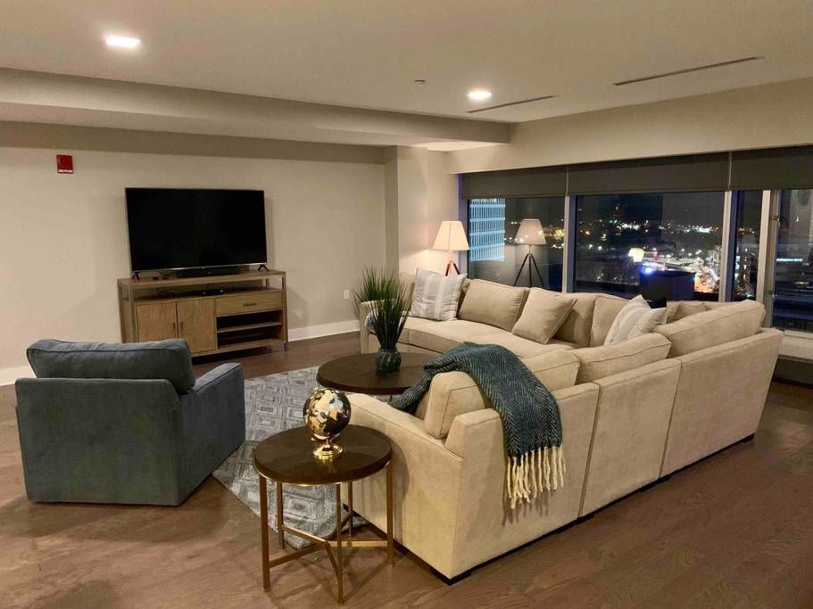Living room with beige sectional, arm chair, TV, city view at night.