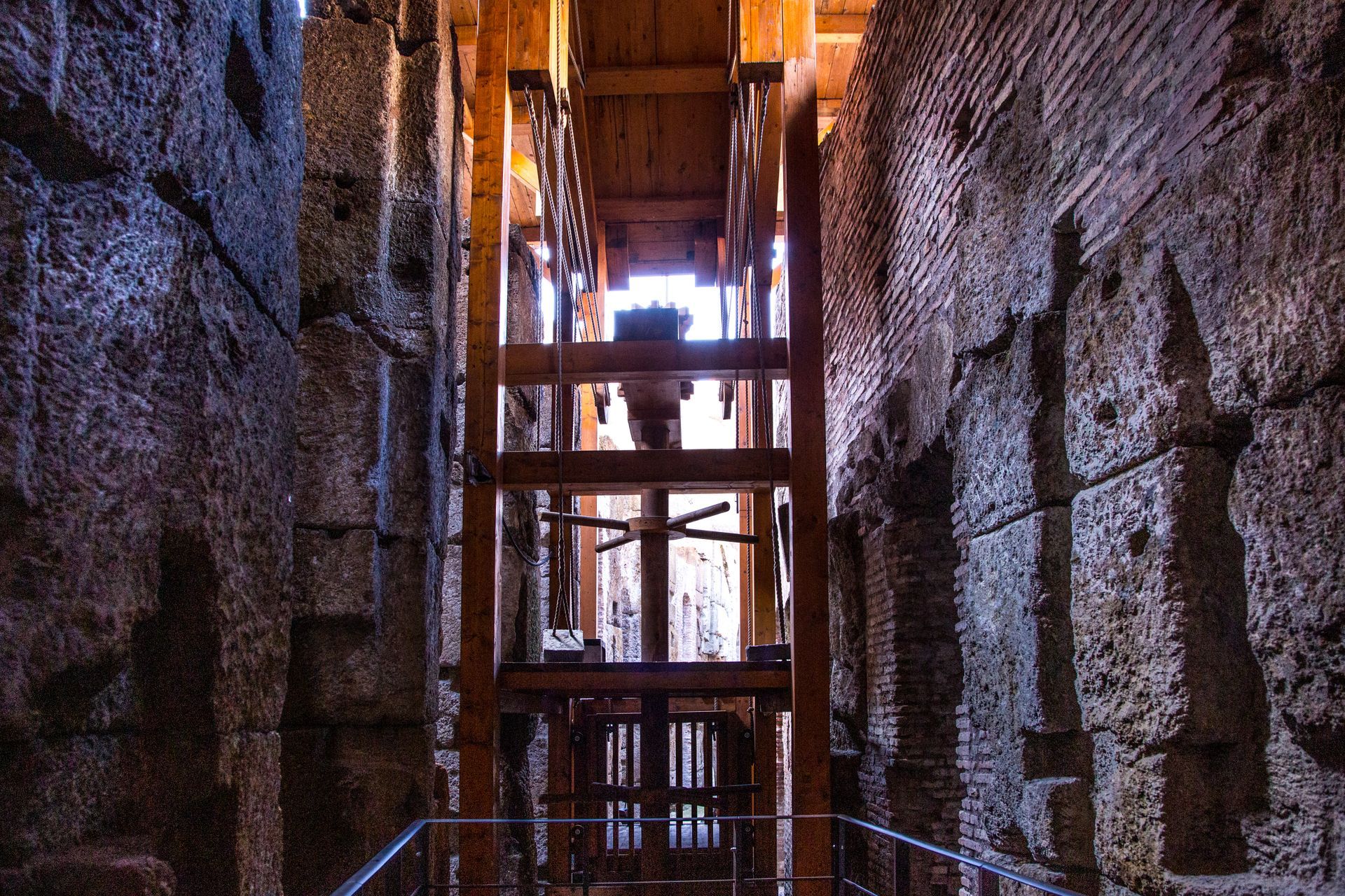 Archway view of the Roman Colosseum interior, showing brick walls and stone ruins, with light sky.
