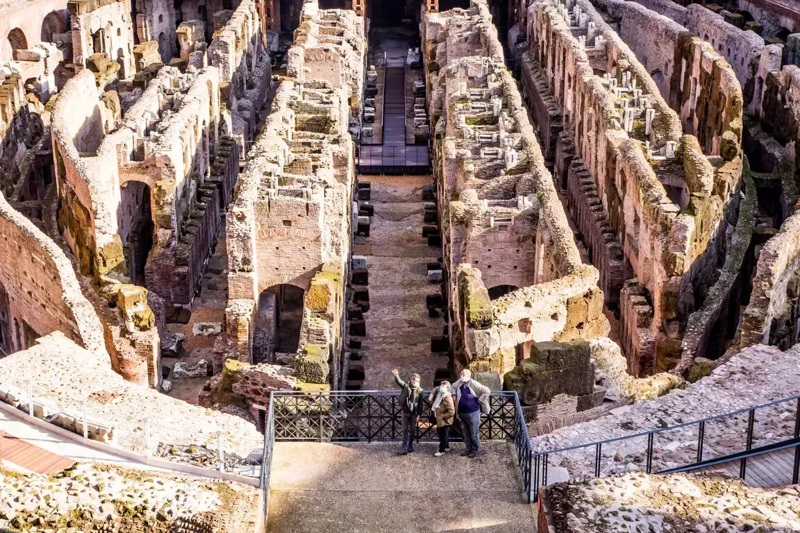 Interior view of the Colosseum in Rome, Italy, with ruins of arches and passageways. Two people stand on a viewing platform.