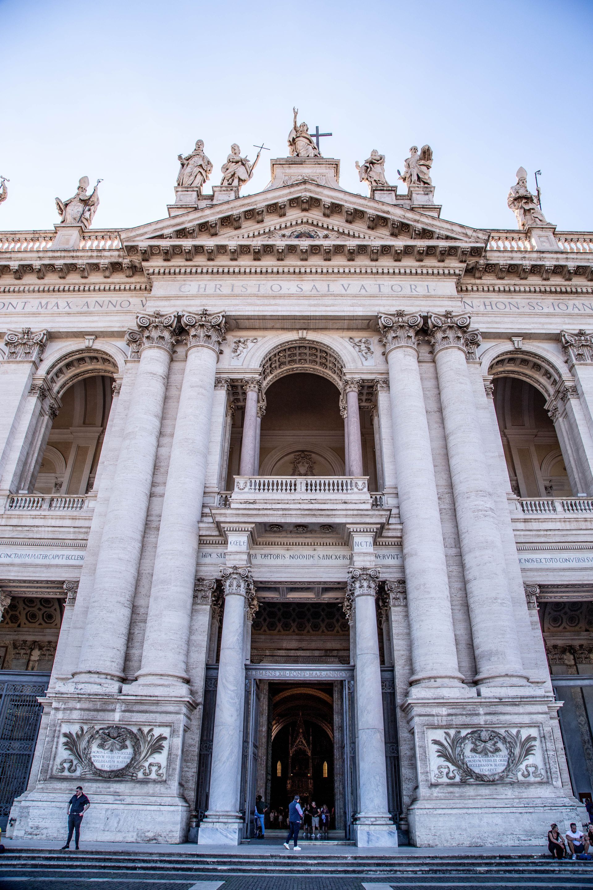White and tan facade of the Archbasilica of St. John Lateran, Rome, with statues on top.