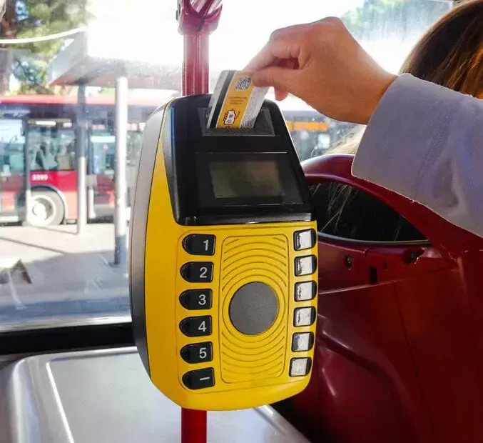 Hand tapping a transit card on a yellow fare reader inside a bus.