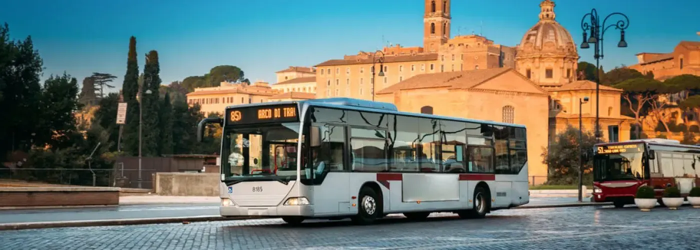 Bus on cobblestone road in front of historical buildings. Blue sky.