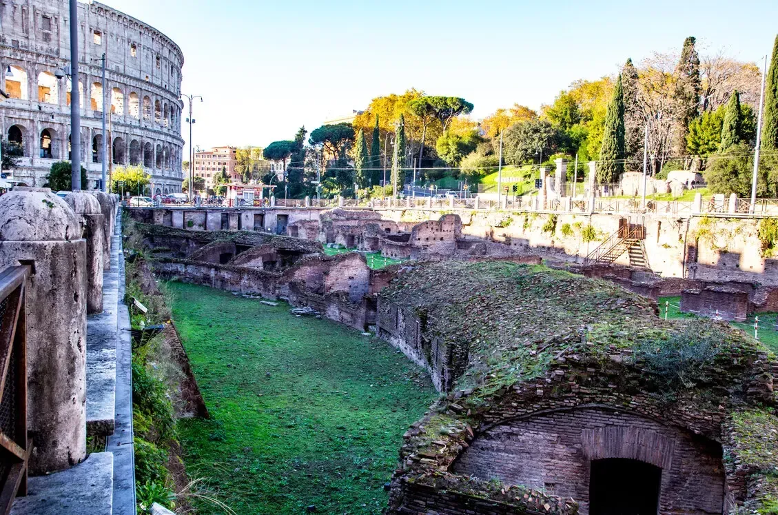 Colosseum and Roman Forum ruins, Rome, Italy. Sunlight illuminates ancient structures and green grass.