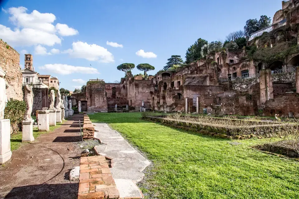Ruins of ancient Roman structures with statues, a lawn, and clear blue sky.