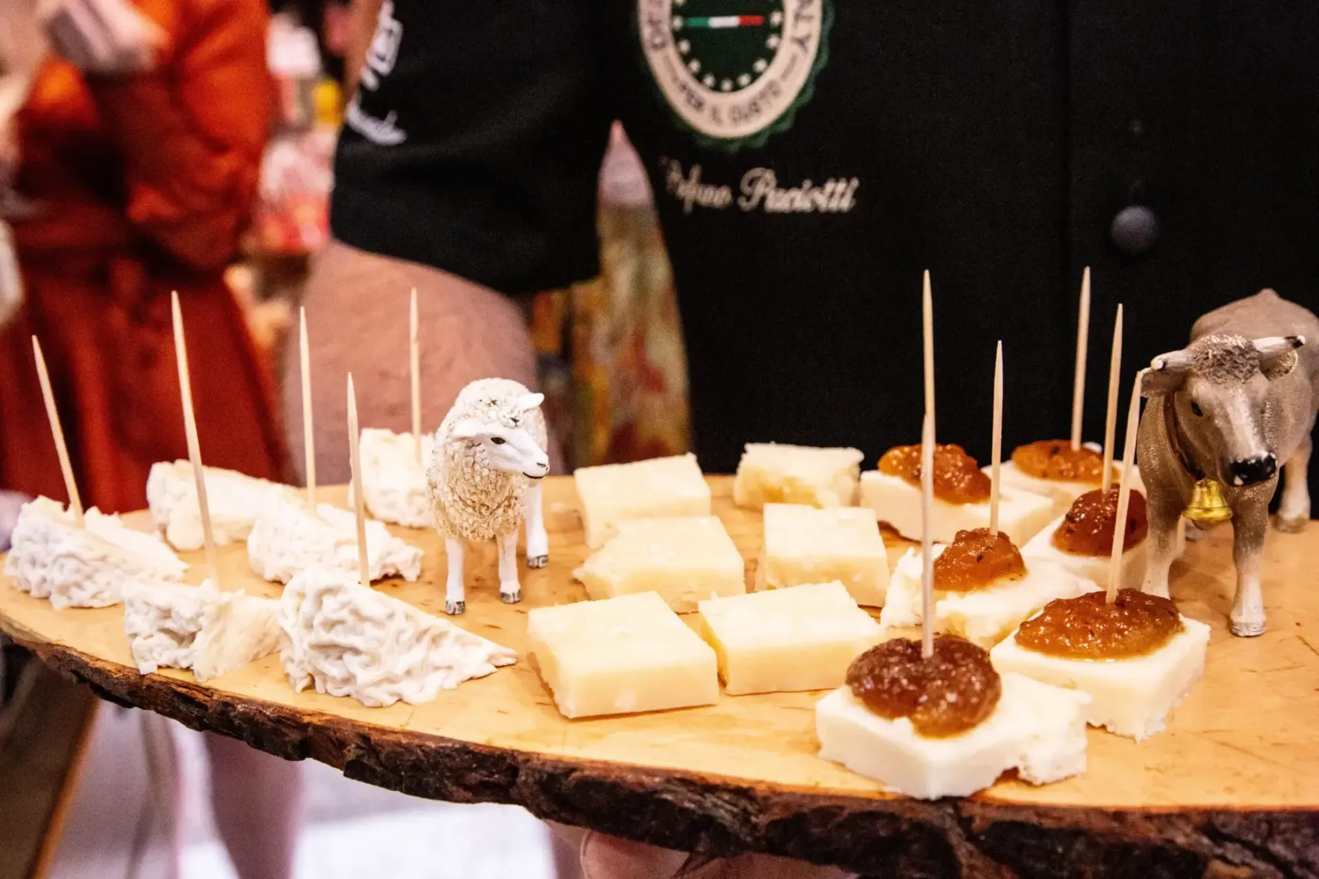 Wooden platter of cheese cubes and appetizers held by a person.