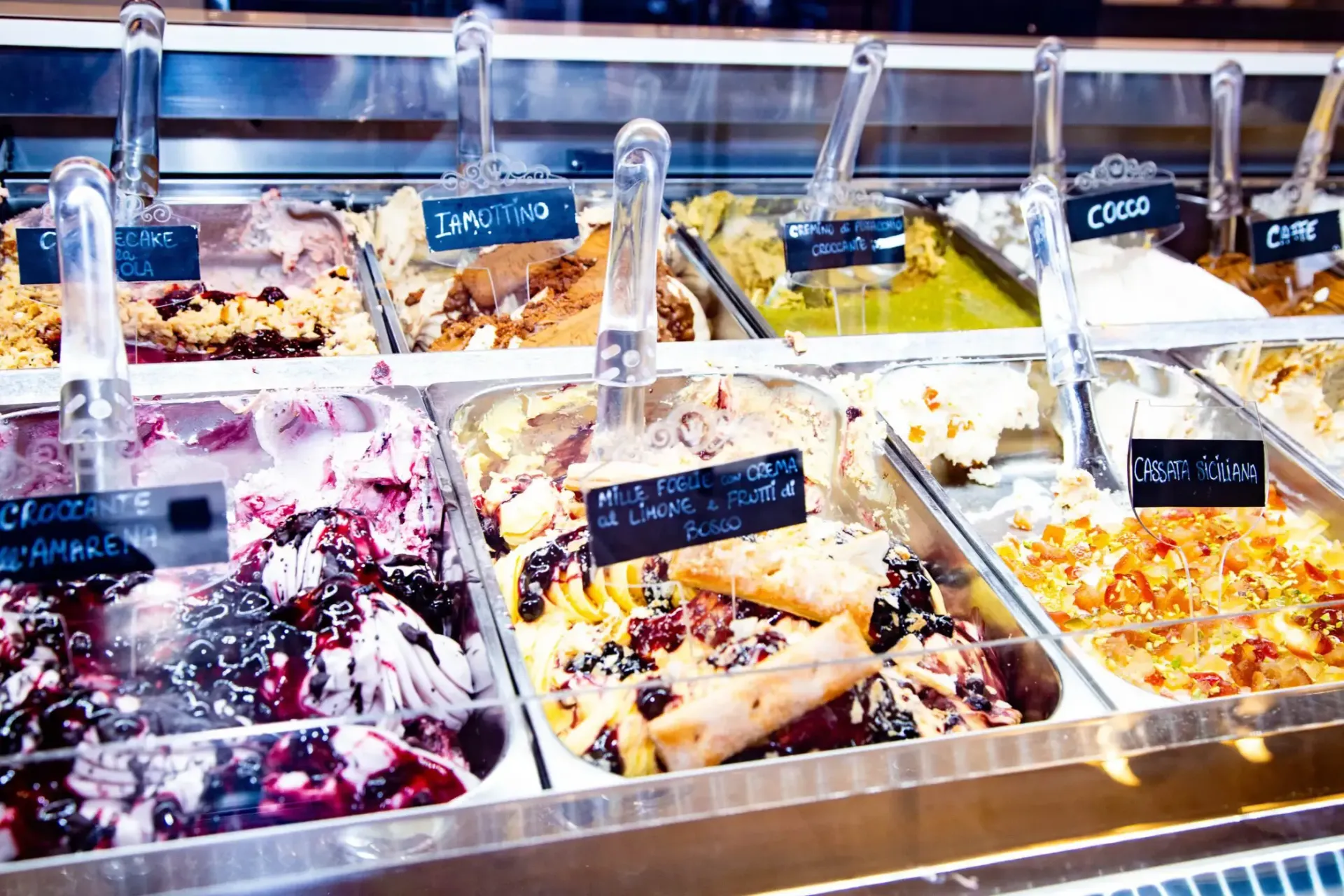 Gelato display case with various colorful flavors, including berry, pistachio, and chocolate.