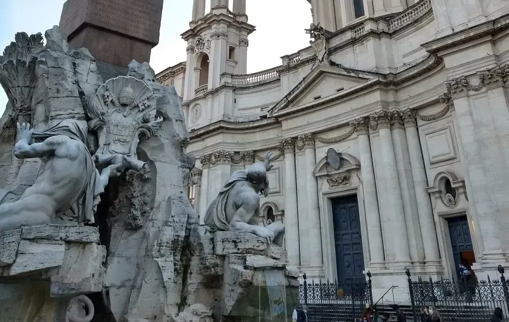 Fountain with statues in front of a white church in Rome.