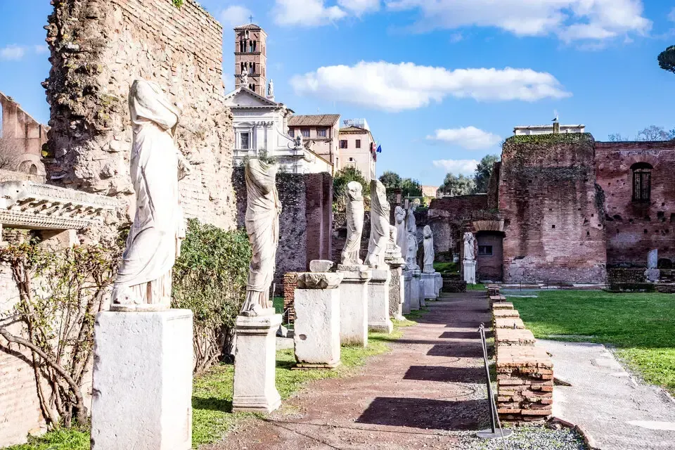 Row of white statues on pedestals in ancient Roman ruins. Sunny, blue sky, brick and stone structures.
