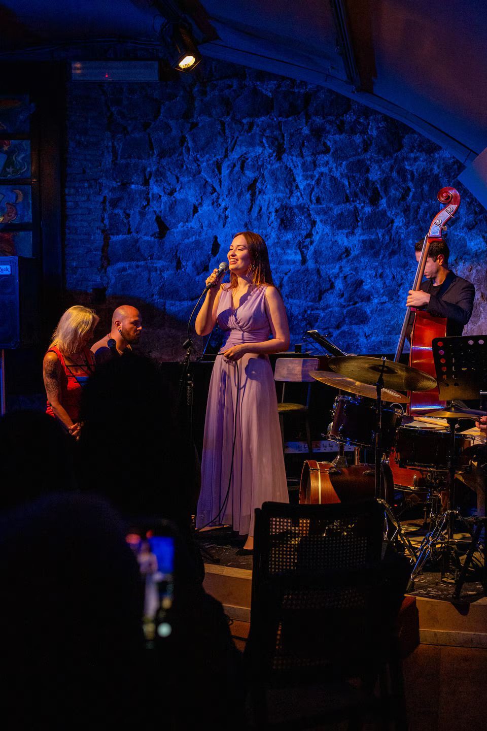 Romantic couple with ancient Roman ruins with tall columns, backlit by the sun, set behind a metal fence and red flowers.