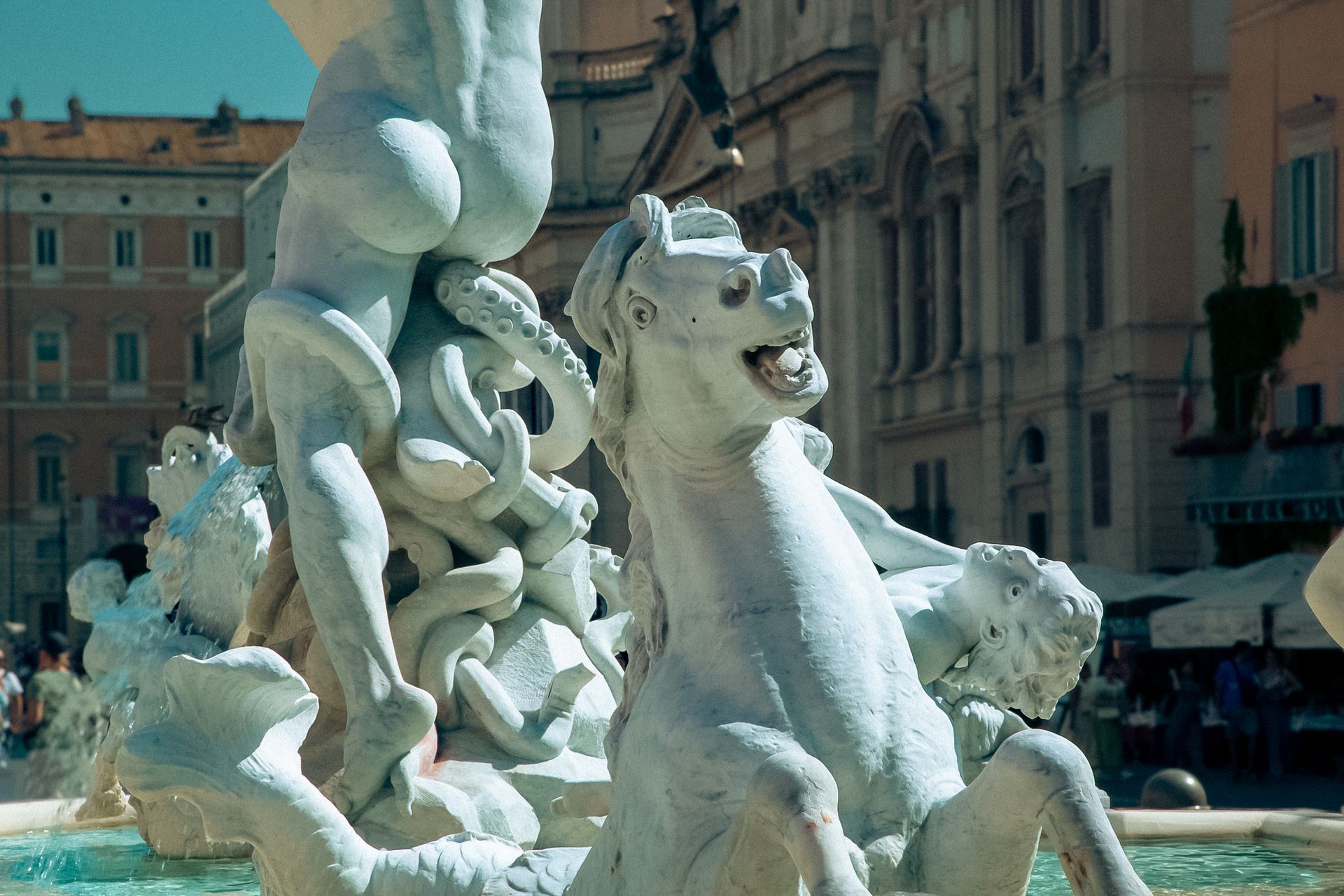 Fountain with statues in front of a white church in Rome.