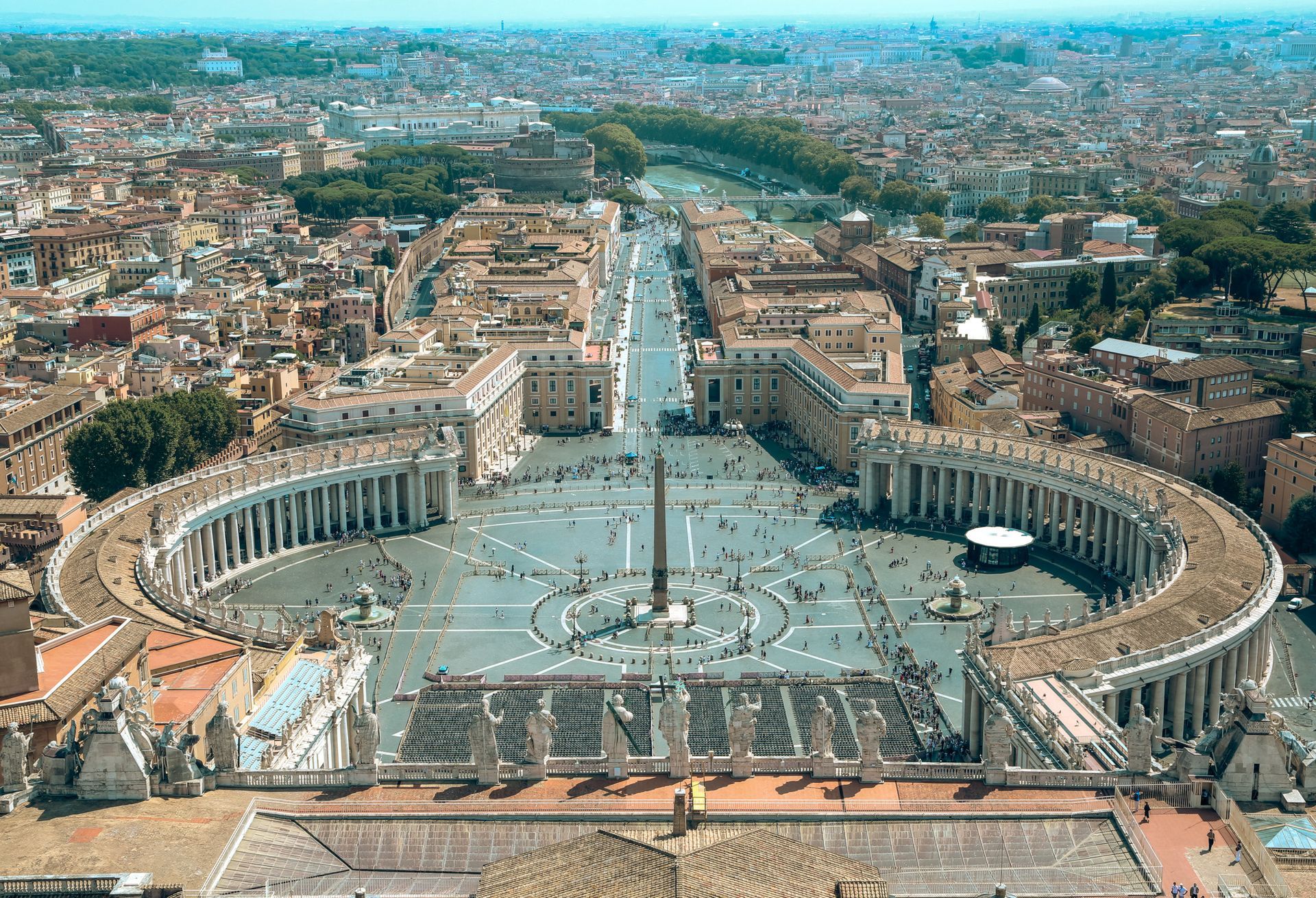 St. Peter's Basilica, Rome, seen from a street lined with columns and streetlights; blue sky above.