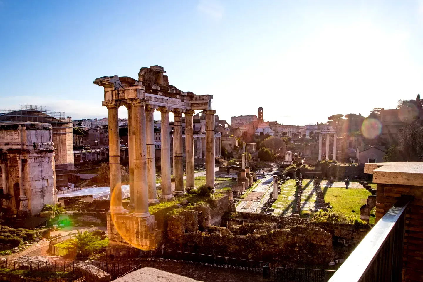 Ancient Roman Forum ruins bathed in sunlight. Columns, crumbling structures, and pathways visible.