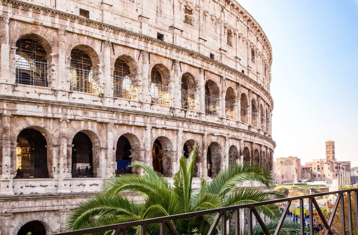 Colosseum in Rome, Italy, with arched windows and a palm tree in the foreground.