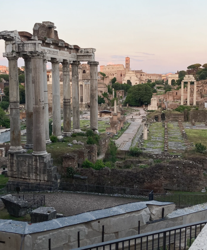 Ancient Roman ruins at sunset, tall columns, stone structures, and pathway visible.