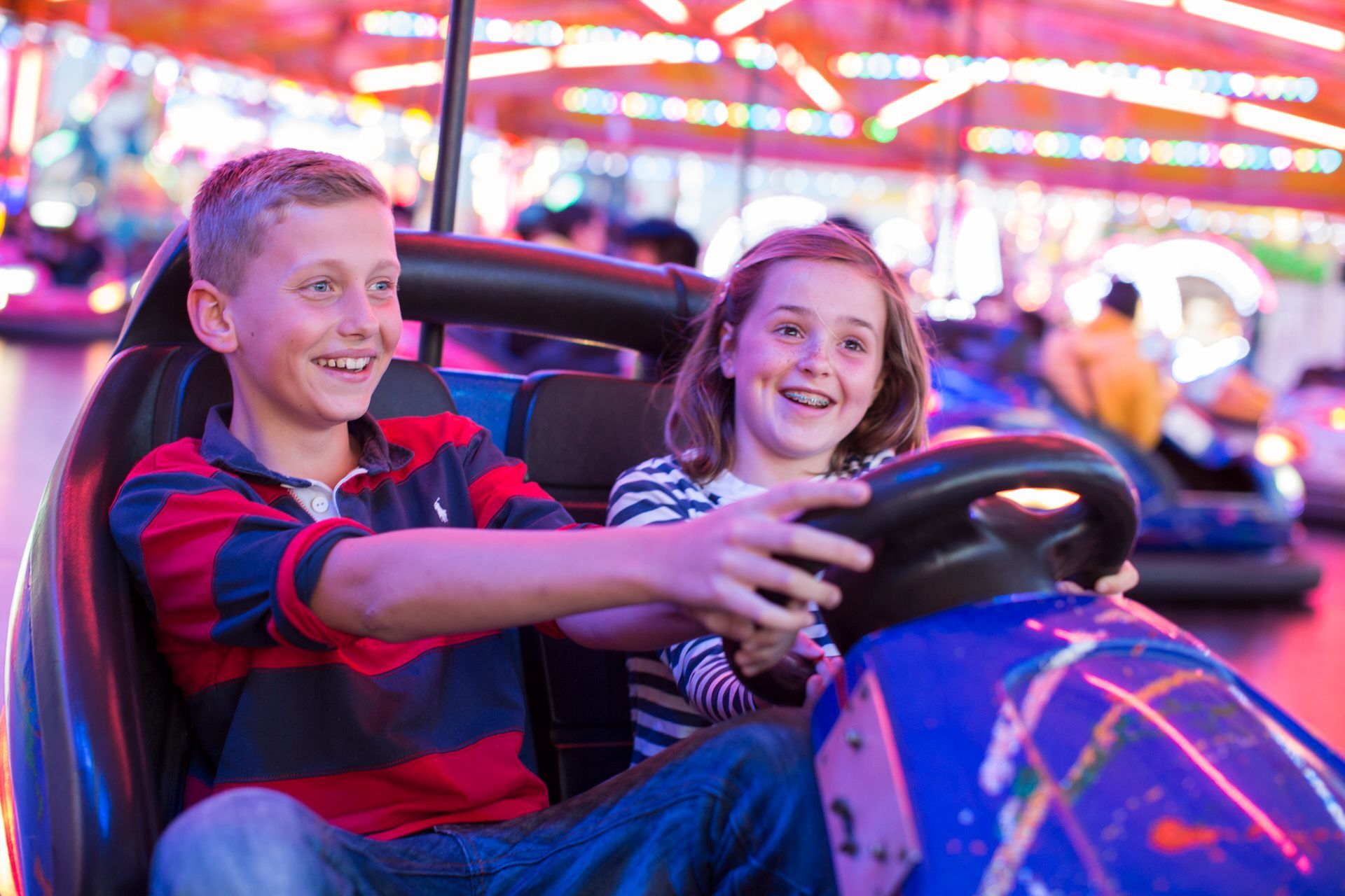 Two children smile while riding bumper cars at an amusement park.