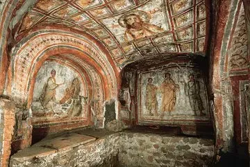 Ancient, frescoed catacomb interior with arched ceilings and religious paintings on the walls and ceiling.