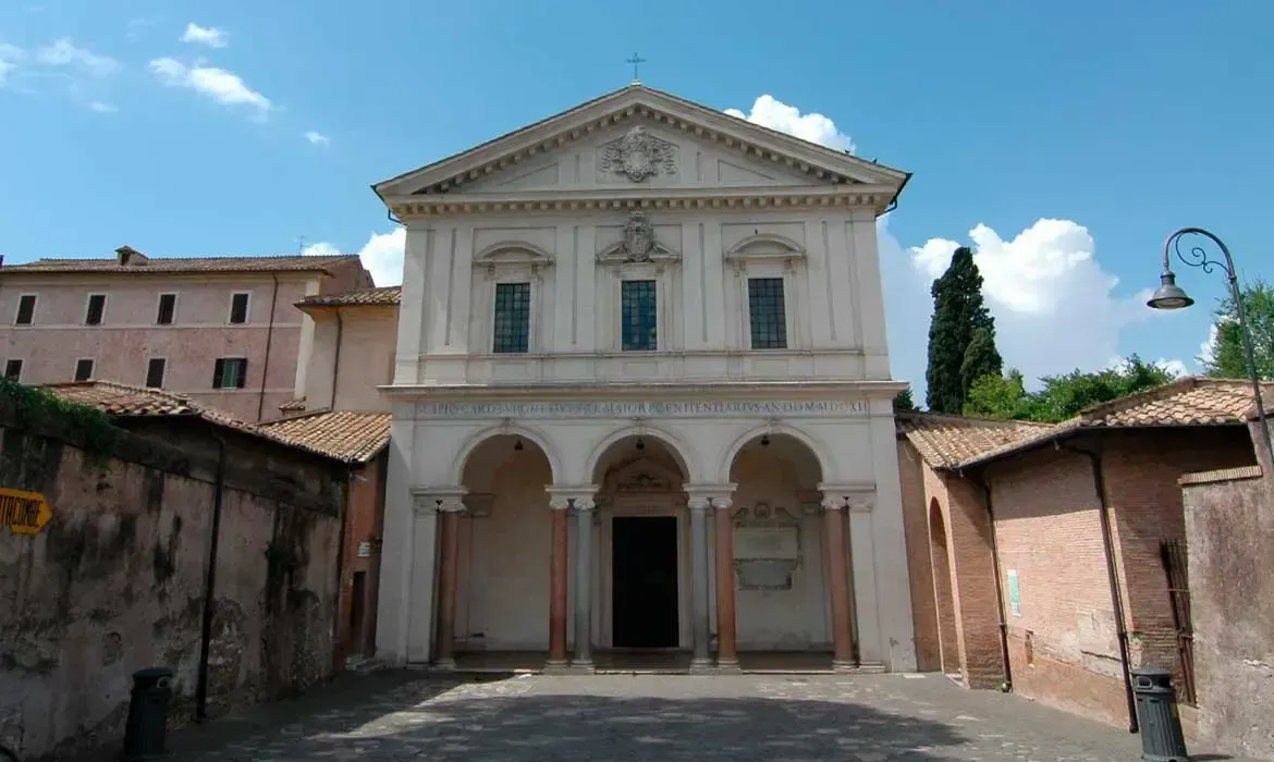 White facade of church with arched entrance and blue sky. Rome.